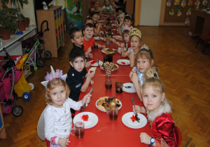 dzieci siedzą przy długim stoliku podczas poczęstunku i jedzą galaretkę